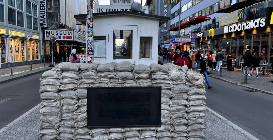 A section of the Berlin Wall with sandbags and a historical marker near Checkpoint Charlie in Berlin.