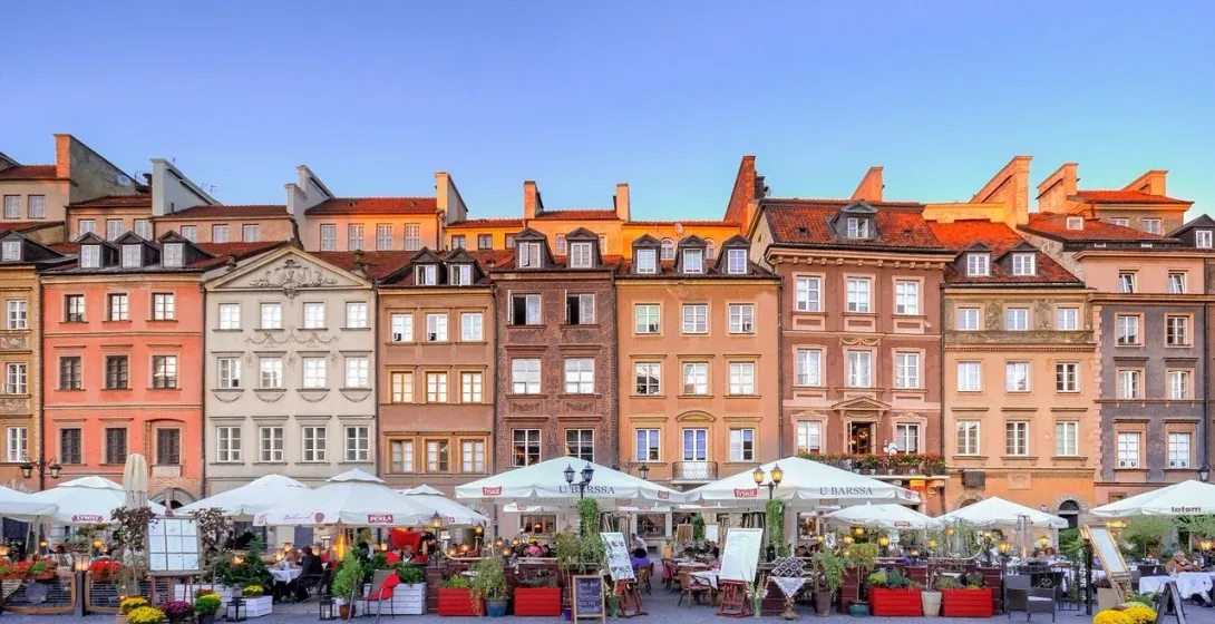 Warsaw's Old Town Square at sunset, featuring colorful buildings and a charming outdoor cafe.