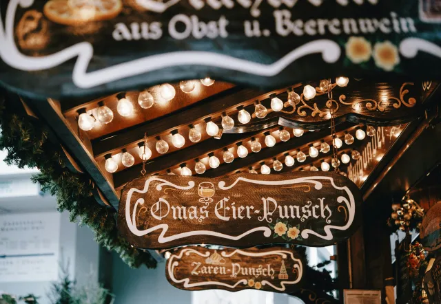 Wooden Christmas market signs advertising Eierpunsch and other drinks decorated with strings of warm lights in Berlin.