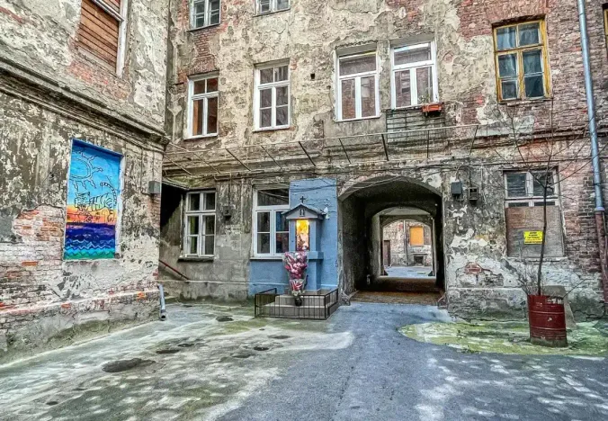 Explore a hidden Warsaw courtyard with aged brick buildings, street art, and a small shrine.