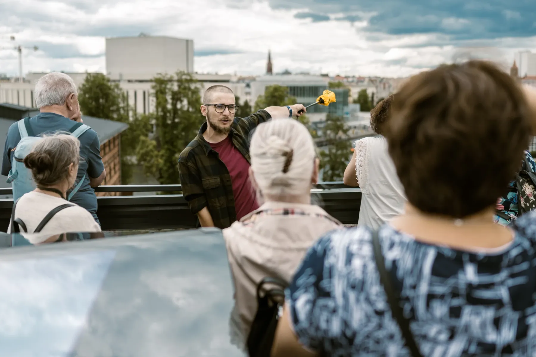 Przewodnik w okularach wskazuje na panoramę Bydgoszczy, wyjaśniając coś niewielkiej grupie turystów.