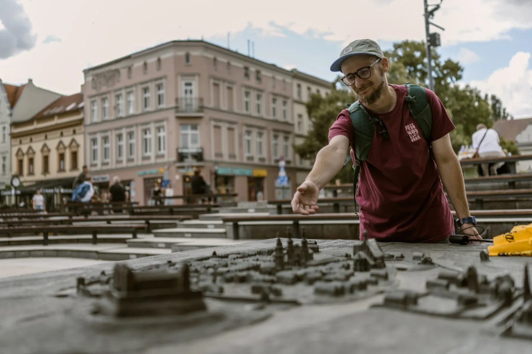 Mężczyzna w czapce i okularach ogląda brązową makietę Starego Miasta, w tle widać kamienice.