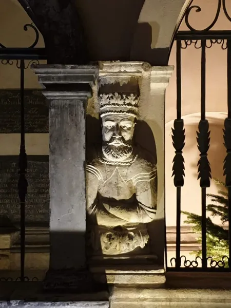 Intricate stone carving of a crowned figure in Krakow at night.