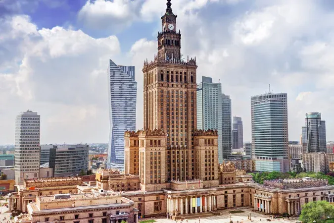 Aerial view of the Palace of Culture and Science and modern skyscrapers under a partly cloudy sky in Warsaw.