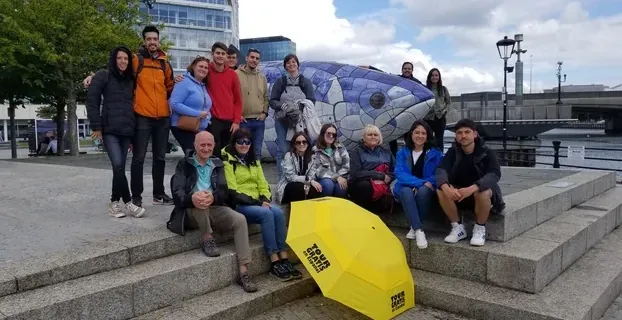 Happy tourists on a free tour of Belfast, posing by a large mosaic fish sculpture.
