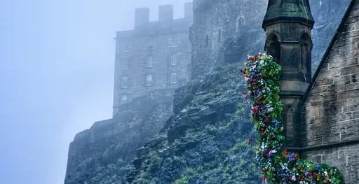 Edinburgh Castle shrouded in fog, with a flower-decorated building in the foreground.