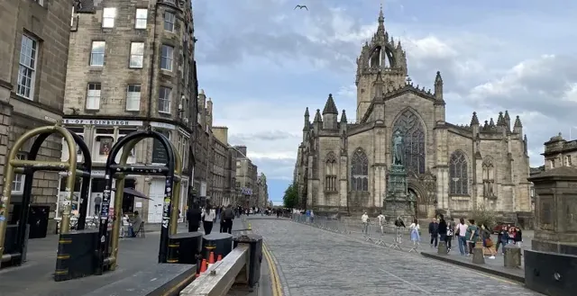 Tourists exploring Edinburgh's Old Town, with St. Giles' Cathedral in the background.