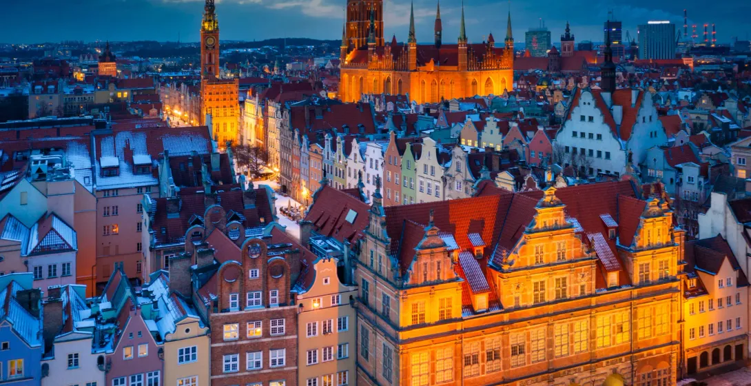 Enchanting twilight view of Gdansk's Old Town, Poland, with snow-dusted rooftops and illuminated historic buildings.