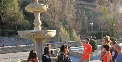 A tour group listens attentively to their guide in Granada, Spain, with the Alhambra Palace in the background.