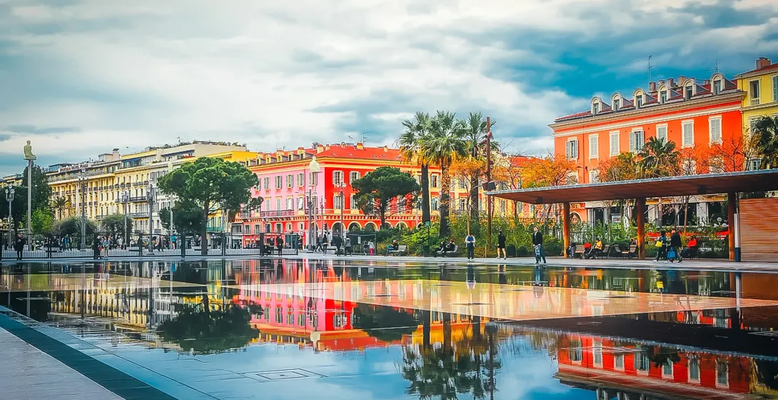 Colorful buildings reflected in a calm water feature in Nice, France.