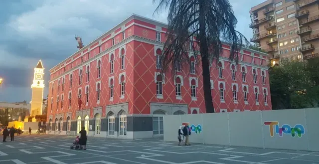 Tourists exploring a vibrant pink building and clock tower in Tirana, Albania.