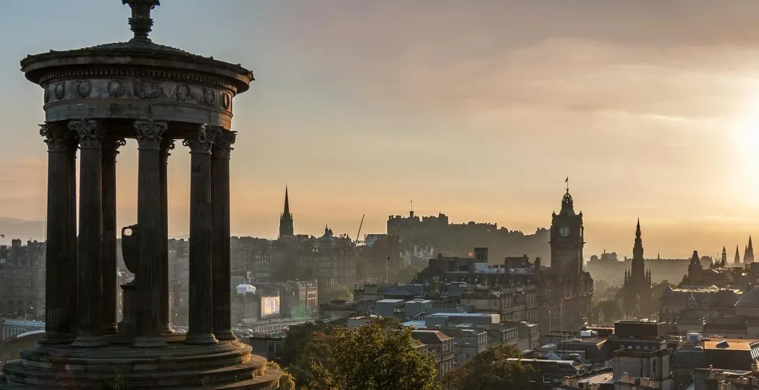 The Dugald Stewart Monument in Edinburgh's Calton Hill at sunrise, overlooking the city skyline with castle and monuments.
