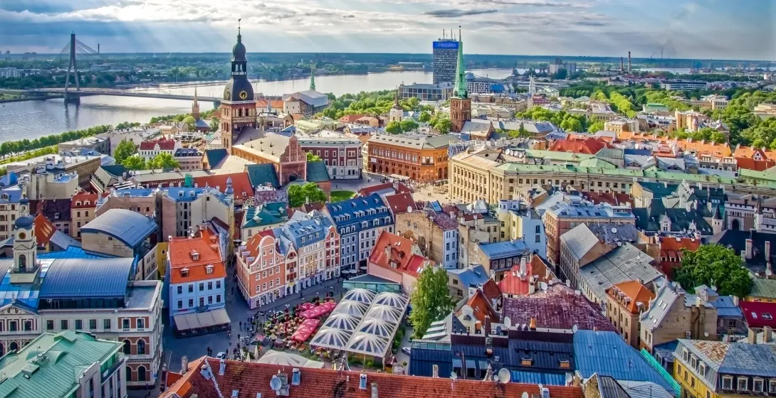 Aerial view of Riga Old Town with colorful buildings, St. Peter's Church spire, Daugava River, and Vansu Bridge under a cloud
