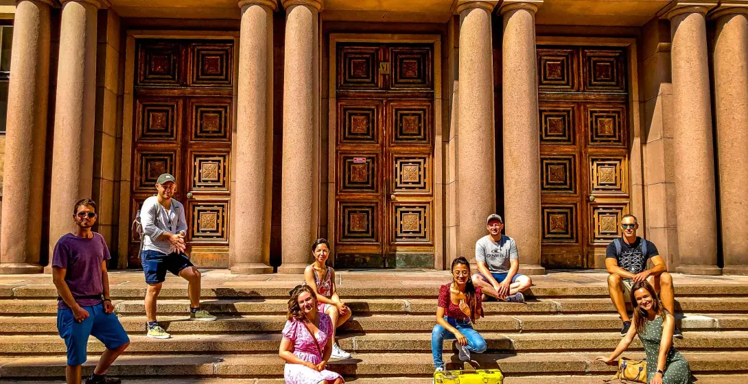 Happy tourists pose on the steps of a beautiful building in Helsinki.