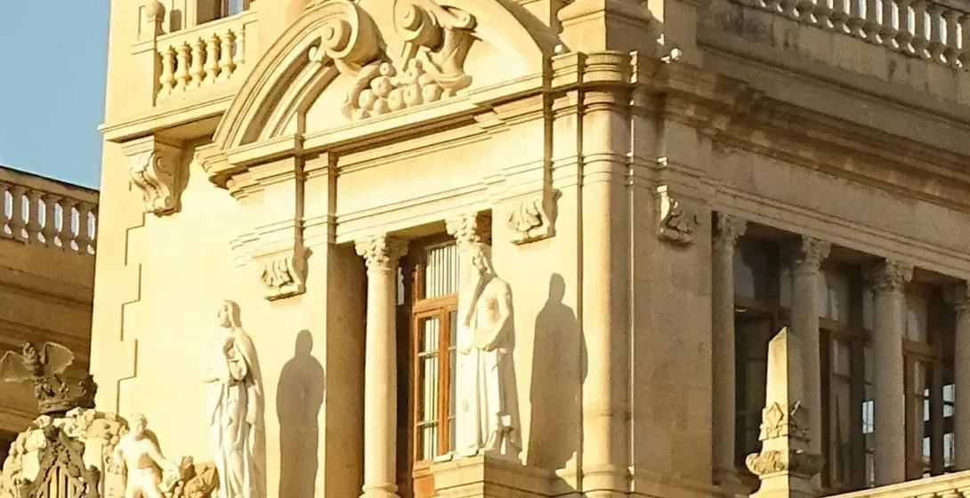Ornate neo-Baroque clock tower of Valencia City Hall under a clear blue sky. Stone facade with columns, statues, and arched w