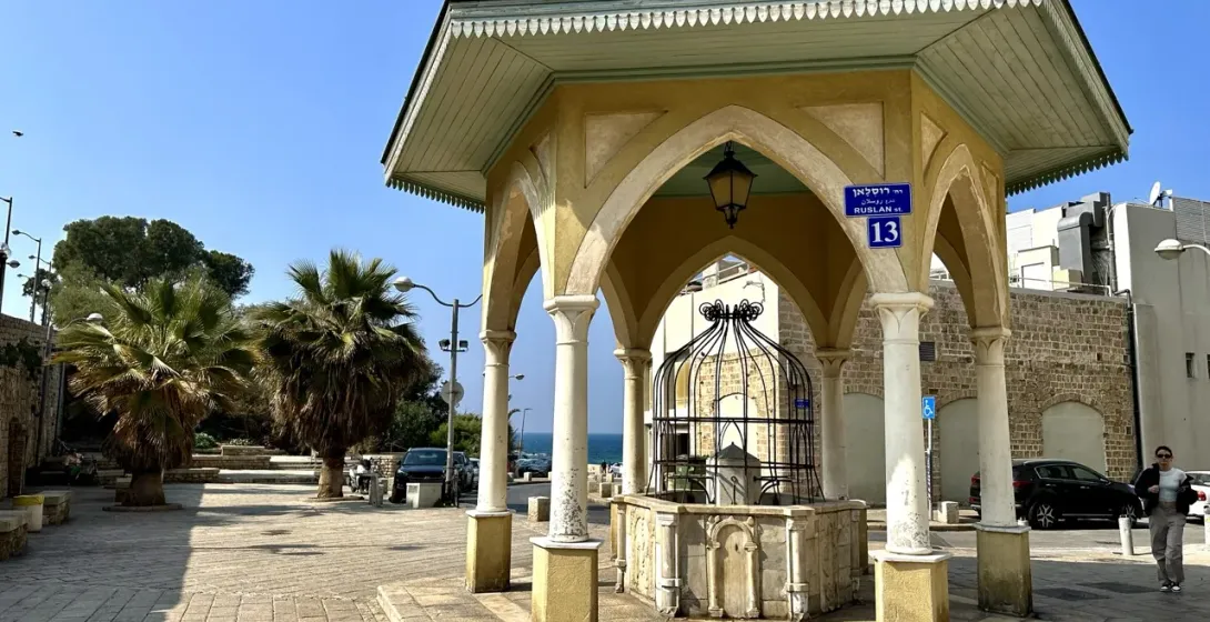 A historical water fountain in a sunlit square in Acre, Israel.