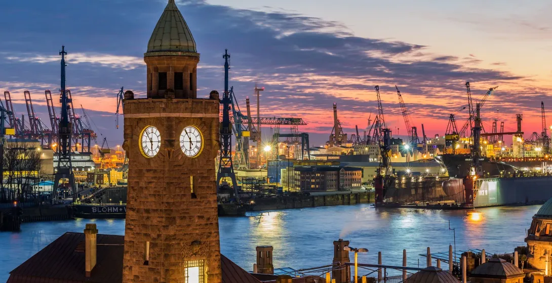 Hamburg harbor at sunset, featuring a clock tower and industrial landscape.
