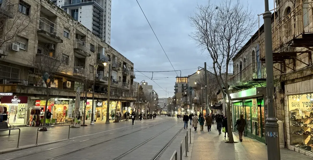 Evening view of a pedestrian street in Jerusalem, with shops and people walking.
