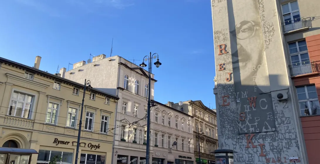 A sunny street scene in Krakow, Poland, featuring a large mural.