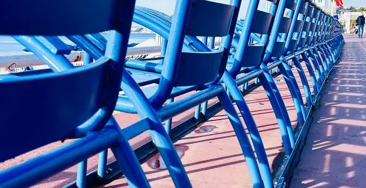 Blue chairs line a promenade in Nice, France, casting long shadows.