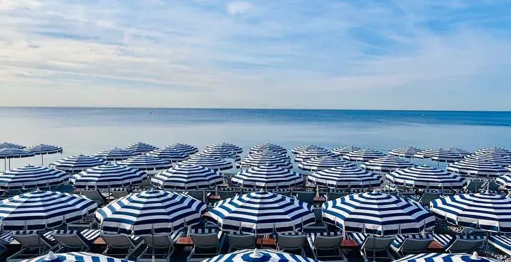 Rows of blue and white striped beach umbrellas and chairs on a Nice beach.