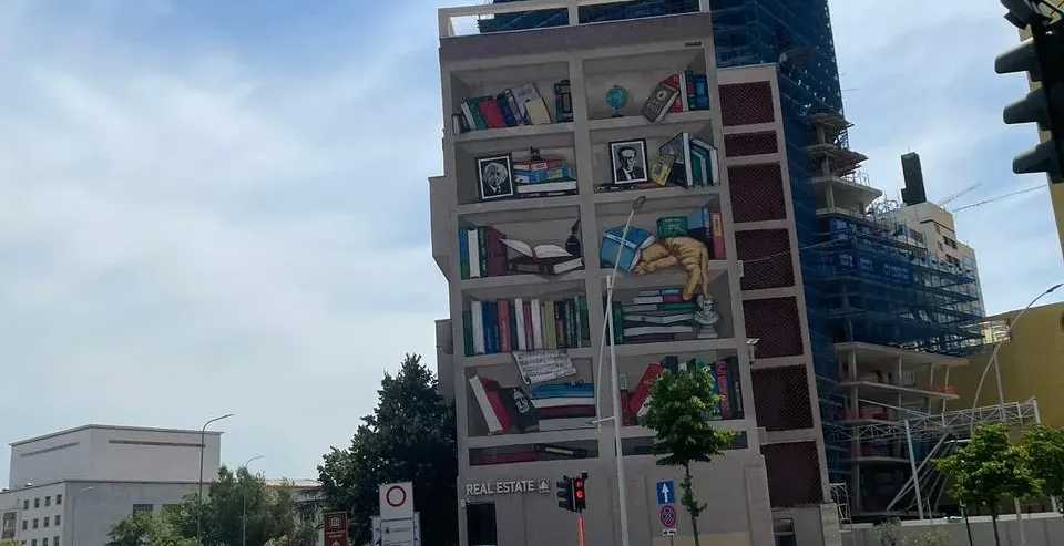 A street scene featuring a building with a large mural of bookshelves.