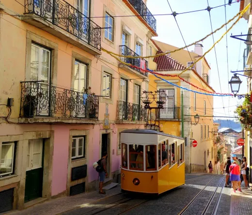 A yellow tram climbs a hill in Lisbon's Alfama & Mouraria districts.