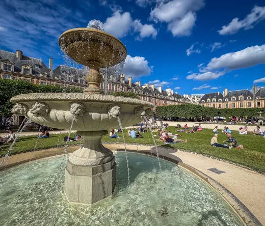 A picturesque fountain in Place des Vosges, Le Marais, Paris, surrounded by people enjoying a sunny day.