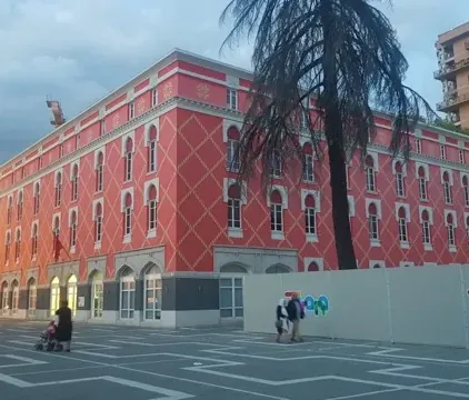 Tourists exploring a vibrant pink building and clock tower in Tirana, Albania.