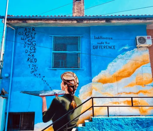 Colorful street art mural of a woman holding a book on a blue building.