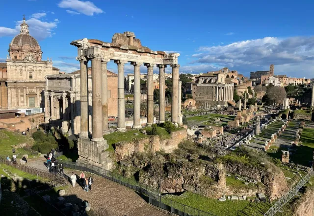 Panoramic view of the Roman Forum in Rome, Italy, with tourists exploring the ancient ruins.