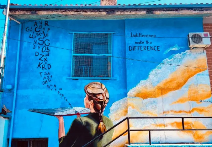 Colorful street art mural of a woman holding a book on a blue building.
