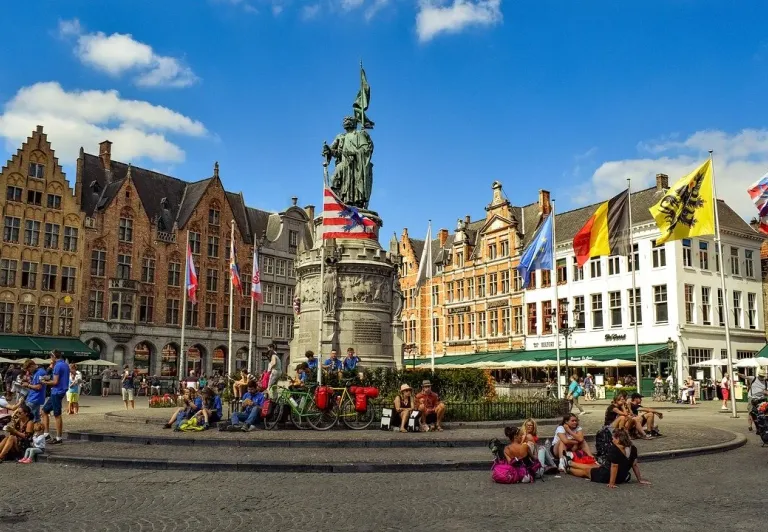 Tourists enjoying the Market Square in Bruges, Belgium, with the Jan van Eyck statue in the background.
