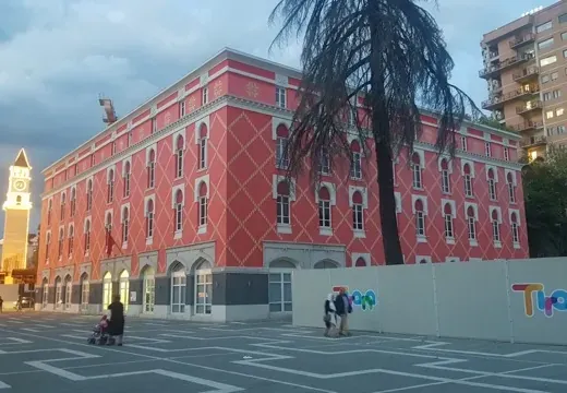 Tourists exploring a vibrant pink building and clock tower in Tirana, Albania.
