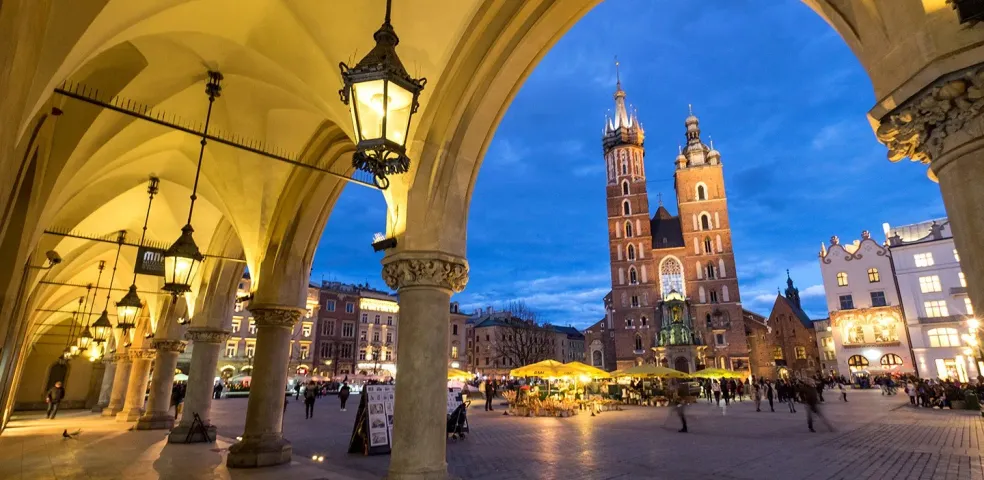 View of St. Mary's Basilica and Krakow Main Market Square at dusk, seen through the illuminated arches of the Sukiennice Clot