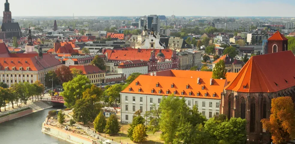Panoramic view of Wroclaw, Poland, featuring the Odra River, historic red-roofed buildings, and city skyline.