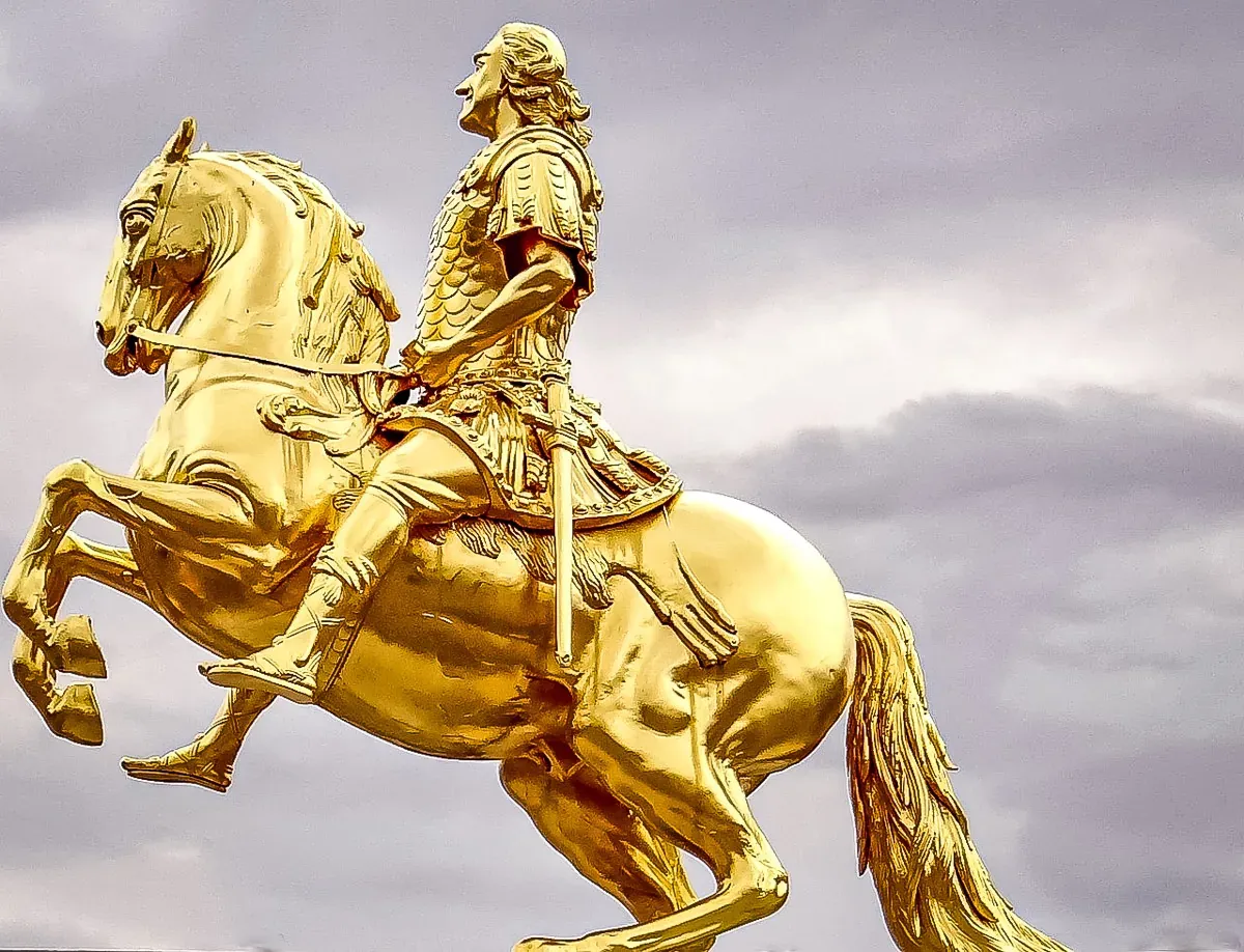 Golden equestrian statue of a man in armor on a rearing horse against a cloudy sky.