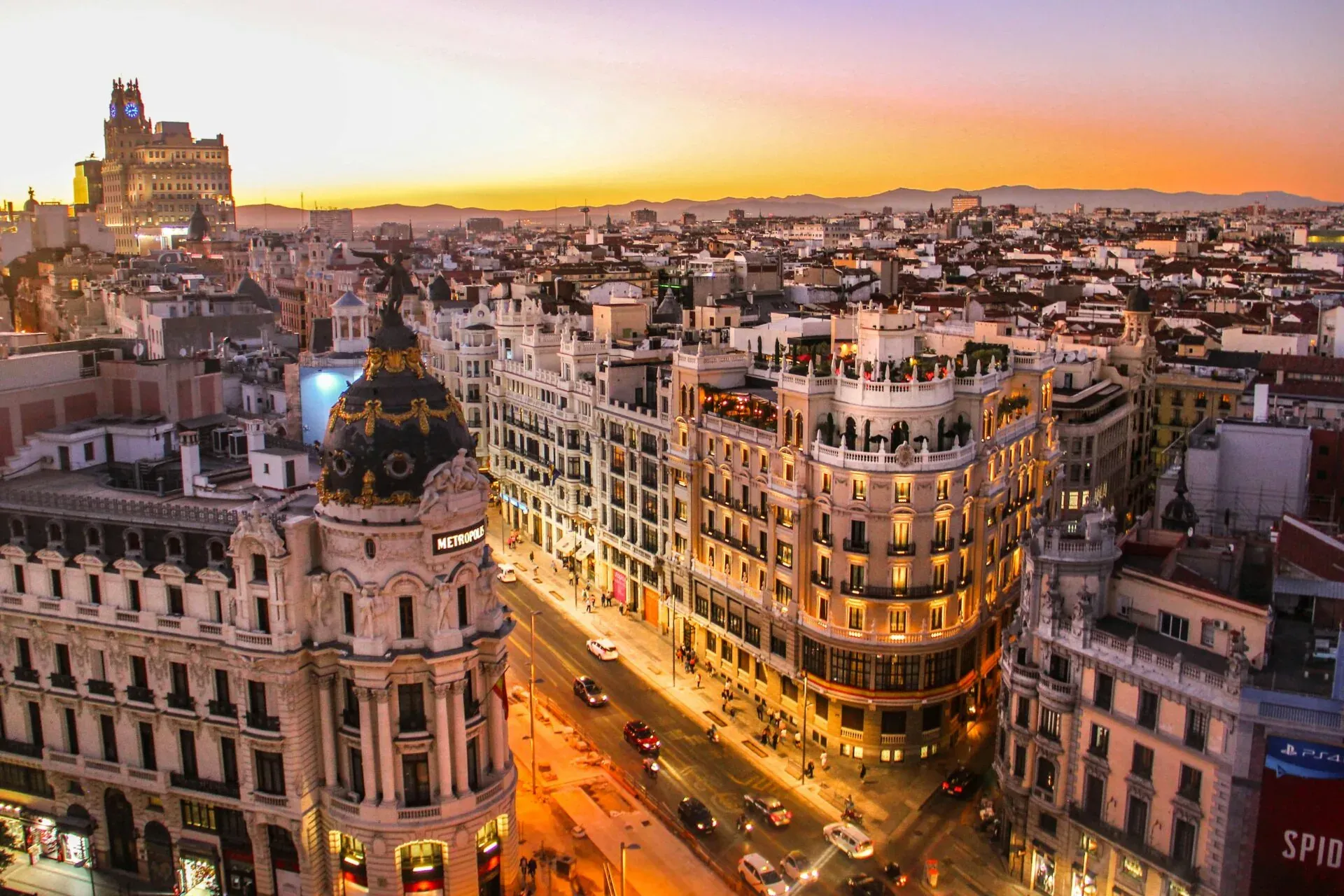 Aerial view of Madrid city at sunset. The ornate Metrópolis Building with its dome is prominent, with cars and pedestrians on