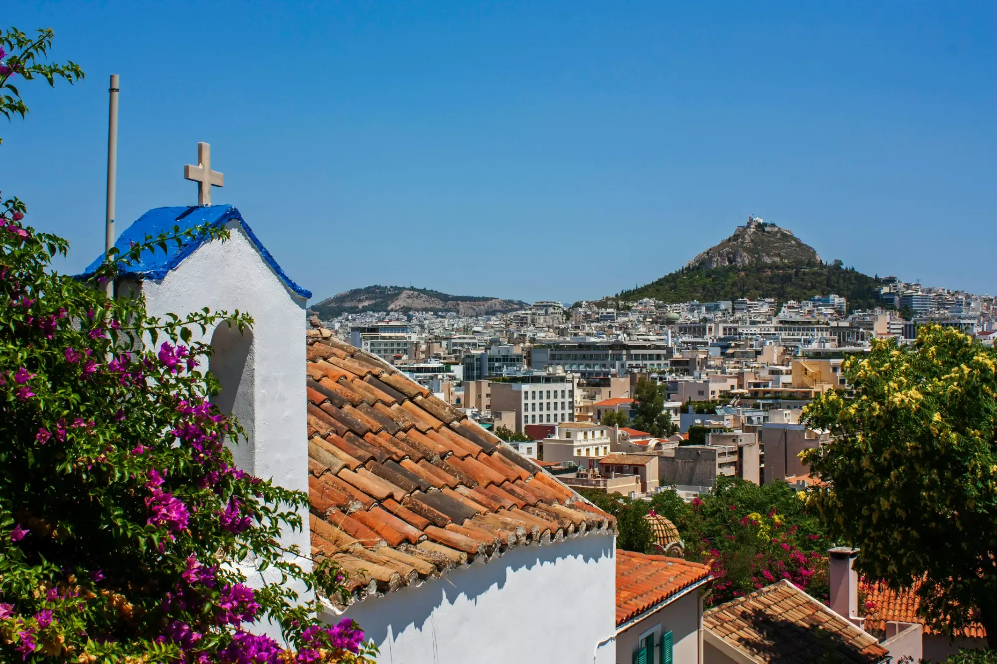 White chapel with a cross and bougainvillea overlooking the city of Athens and Mount Lycabettus.