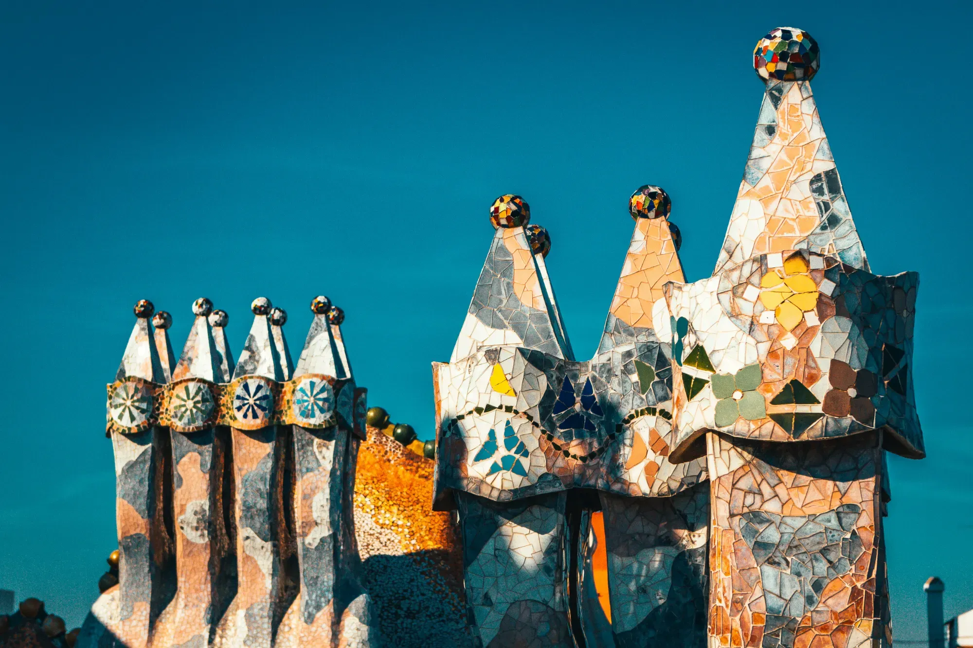 Colorful mosaic-covered chimneys on the rooftop of Palau Güell in Barcelona against a blue sky.
