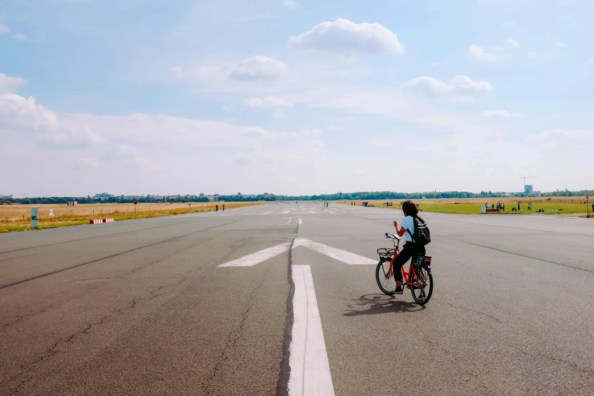 A person riding a red bicycle on the wide runway of Tempelhofer Feld in Berlin on a sunny day.