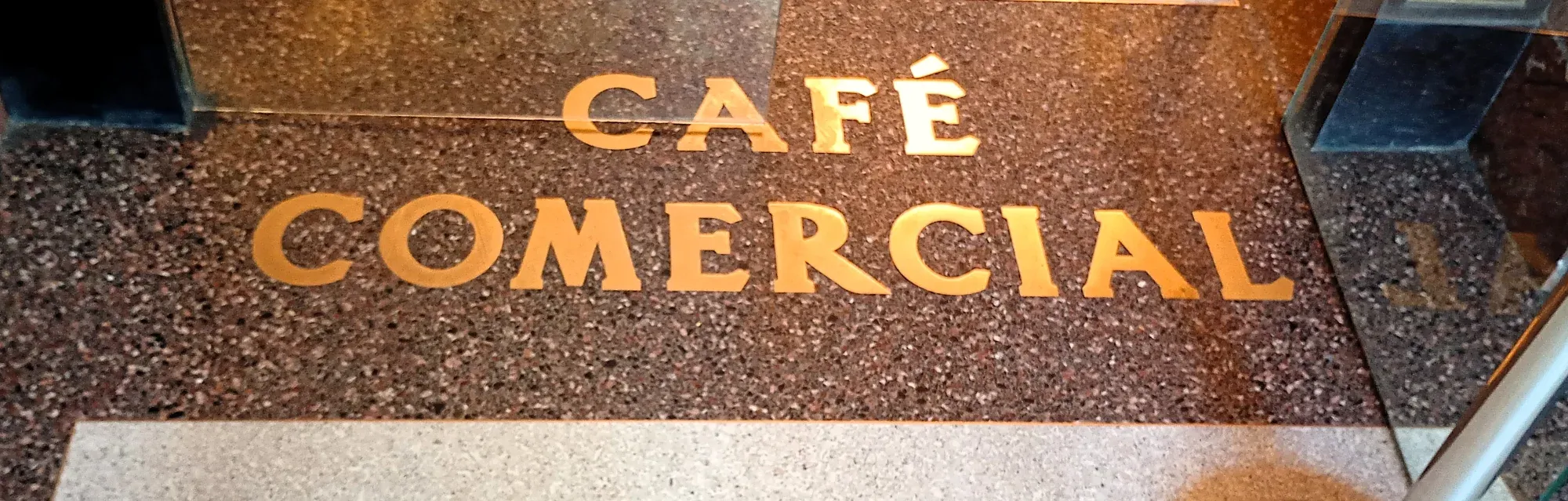 Gold lettering for 'Café Comercial' inlaid in a dark terrazzo floor at the entrance.