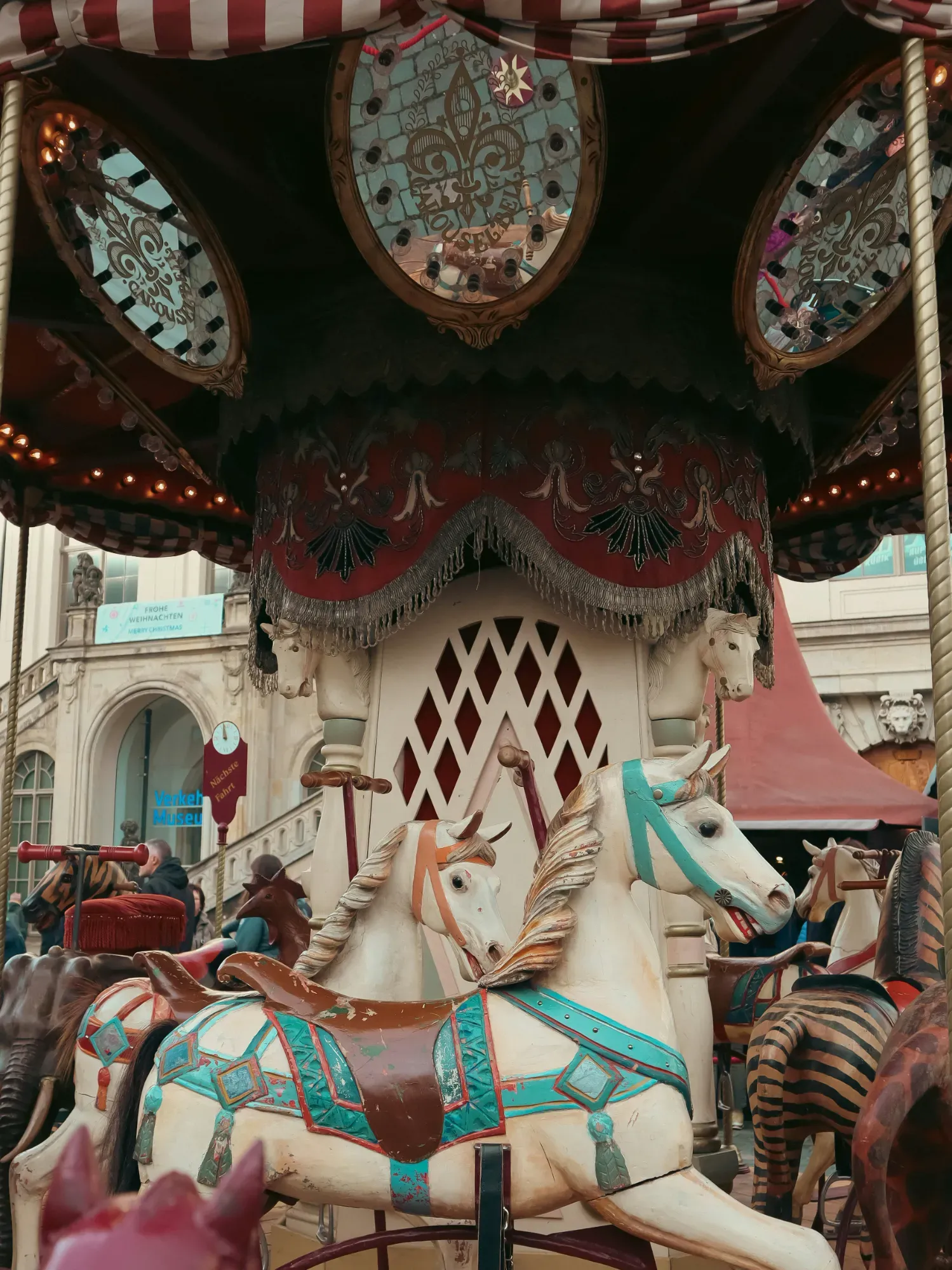 Close-up of vintage carousel, featuring elaborately decorated horses and animals, with historical German architecture in the