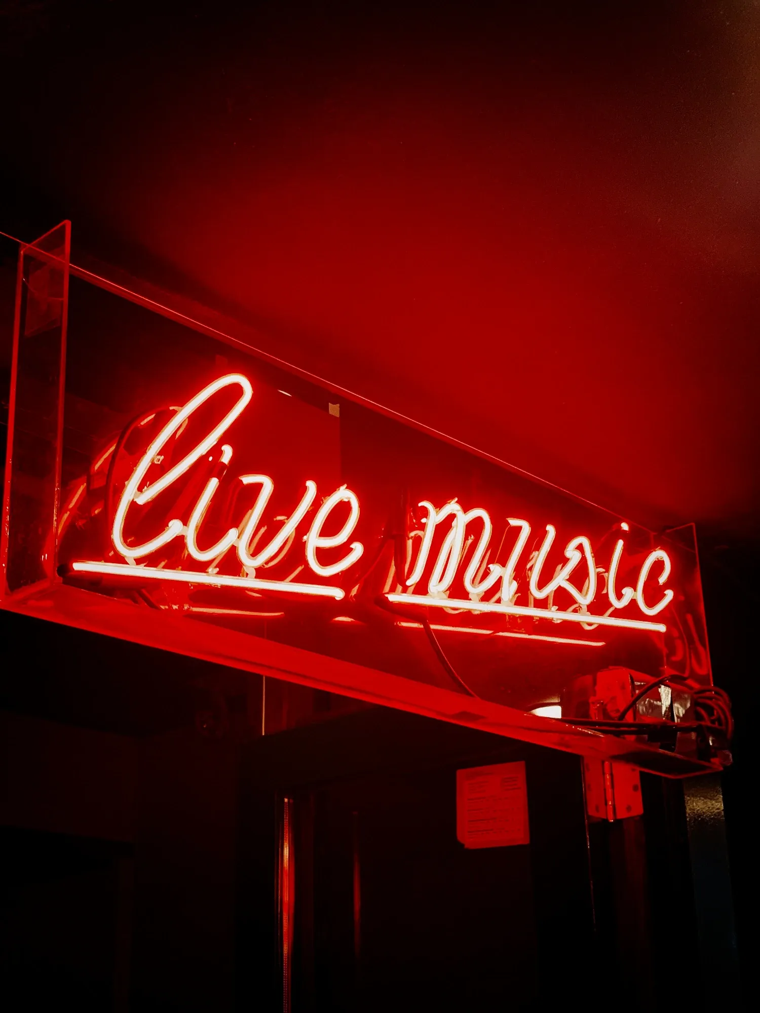 A red neon sign with the words "Live Music" in cursive script, seen from below in a dark room.