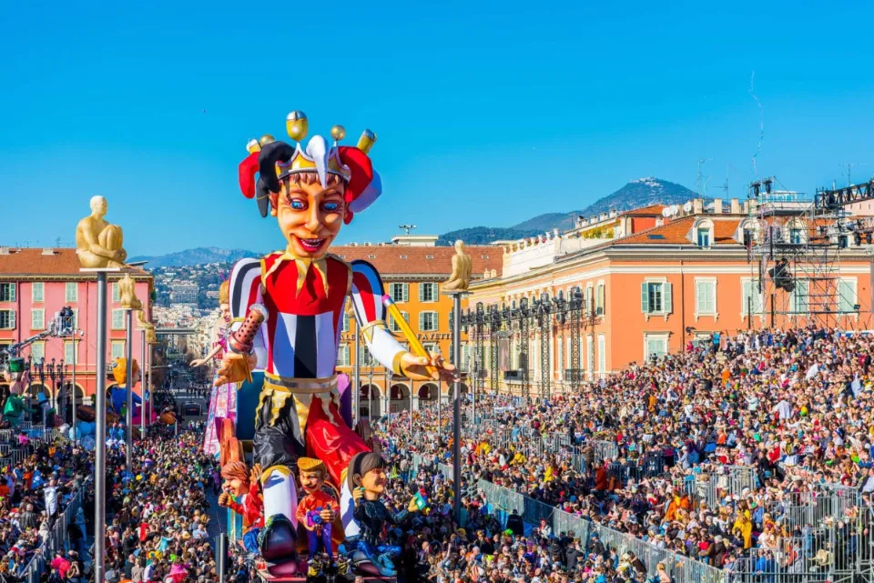 Giant jester float parading through Place Masséna during the Nice Carnival, surrounded by large crowds.