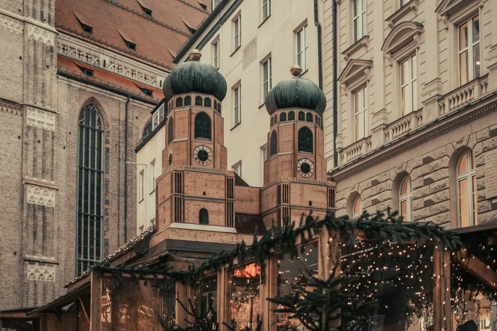 Wooden Christmas market stall topped with miniature towers of the Frauenkirche, framed by historic Munich buildings.