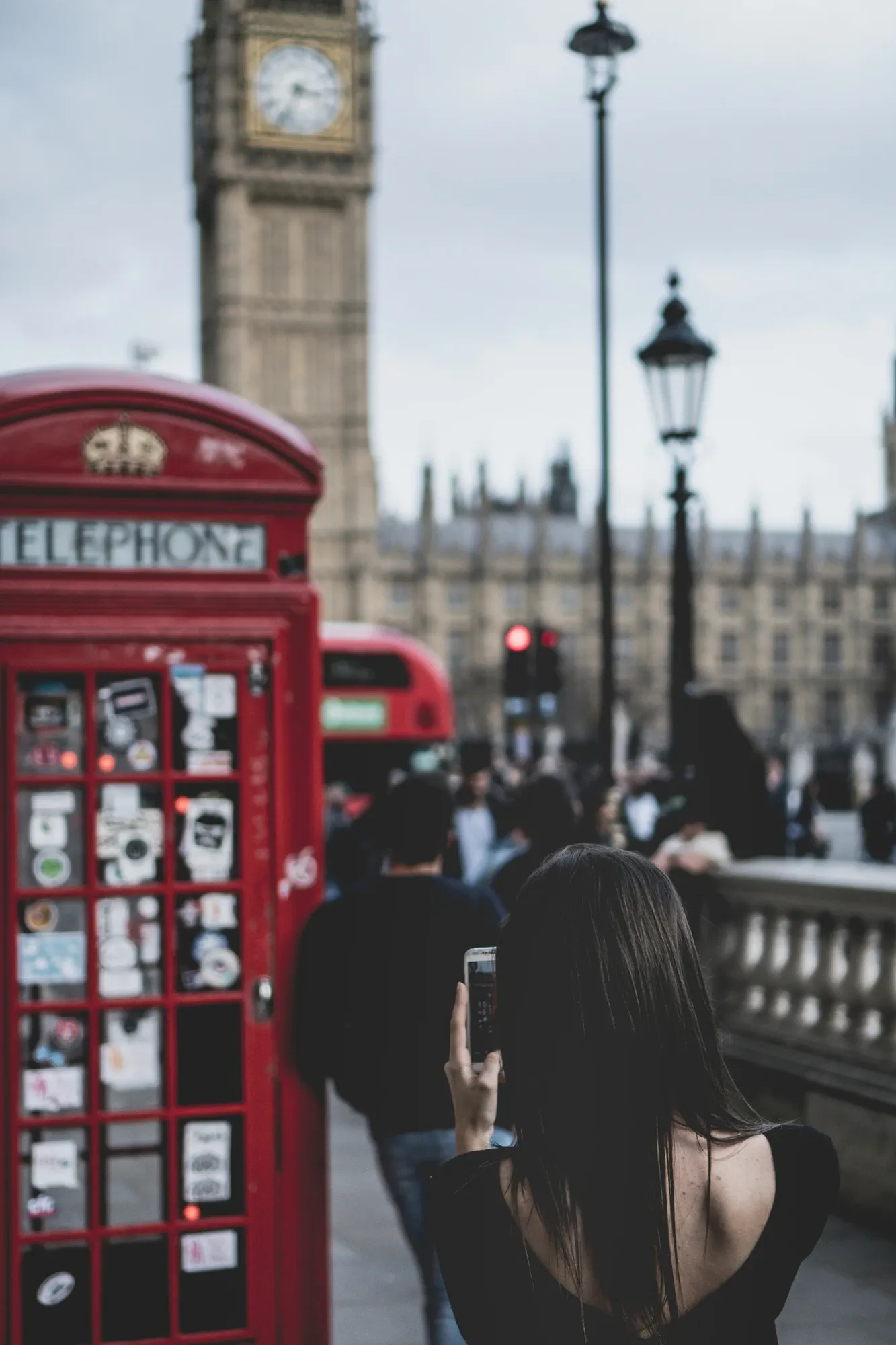 A woman photographs a red telephone box, with the Elizabeth Tower (Big Ben) and Houses of Parliament blurred in the backgr...
