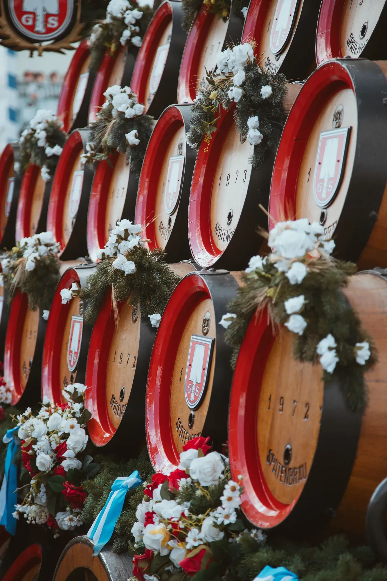 Stack of decorated Spatenbräu brewery wooden beer barrels with red rims, prepared for a festival in Munich.
