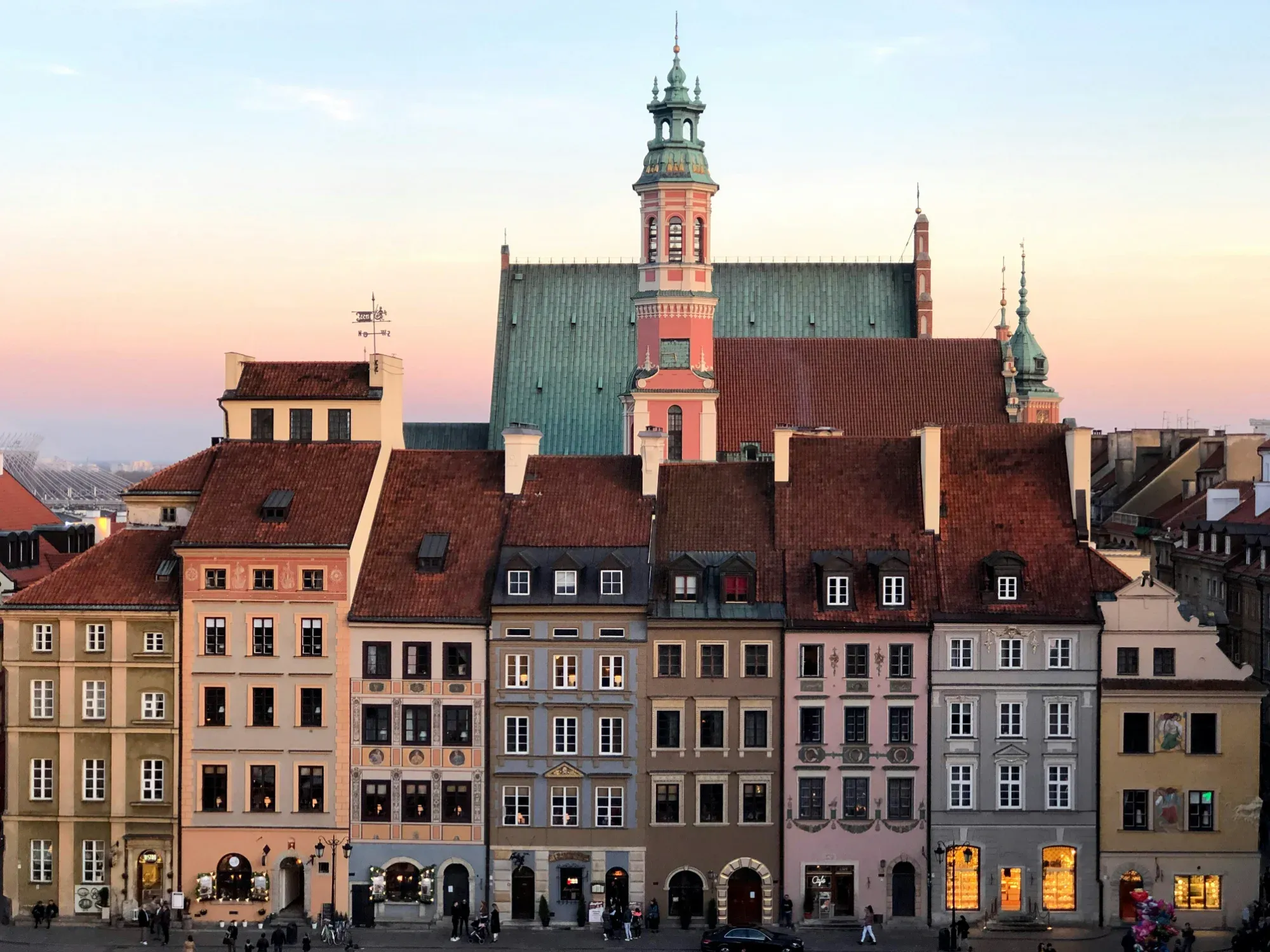 Colorful historic townhouses in Warsaw's Old Town at sunset, with a church tower and stadium in the background.
