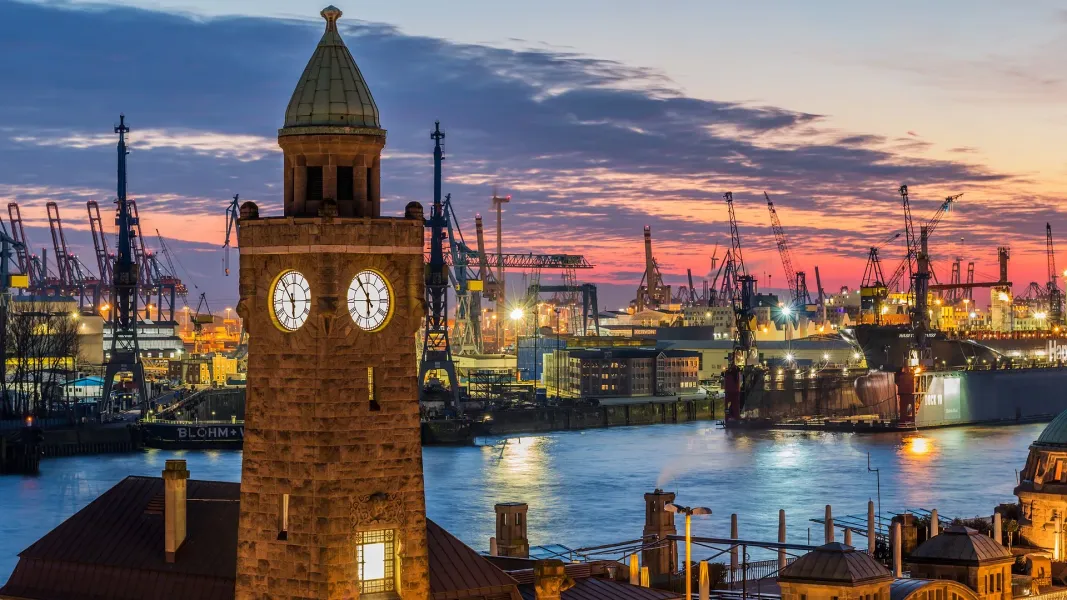 Hamburg harbor at sunset, featuring a clock tower and industrial landscape.